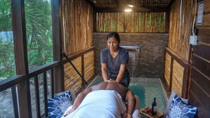 A massage room with a wooden interior, a stone wall, and a view of greenery outside. - Kmar Villas (Maya Beach)