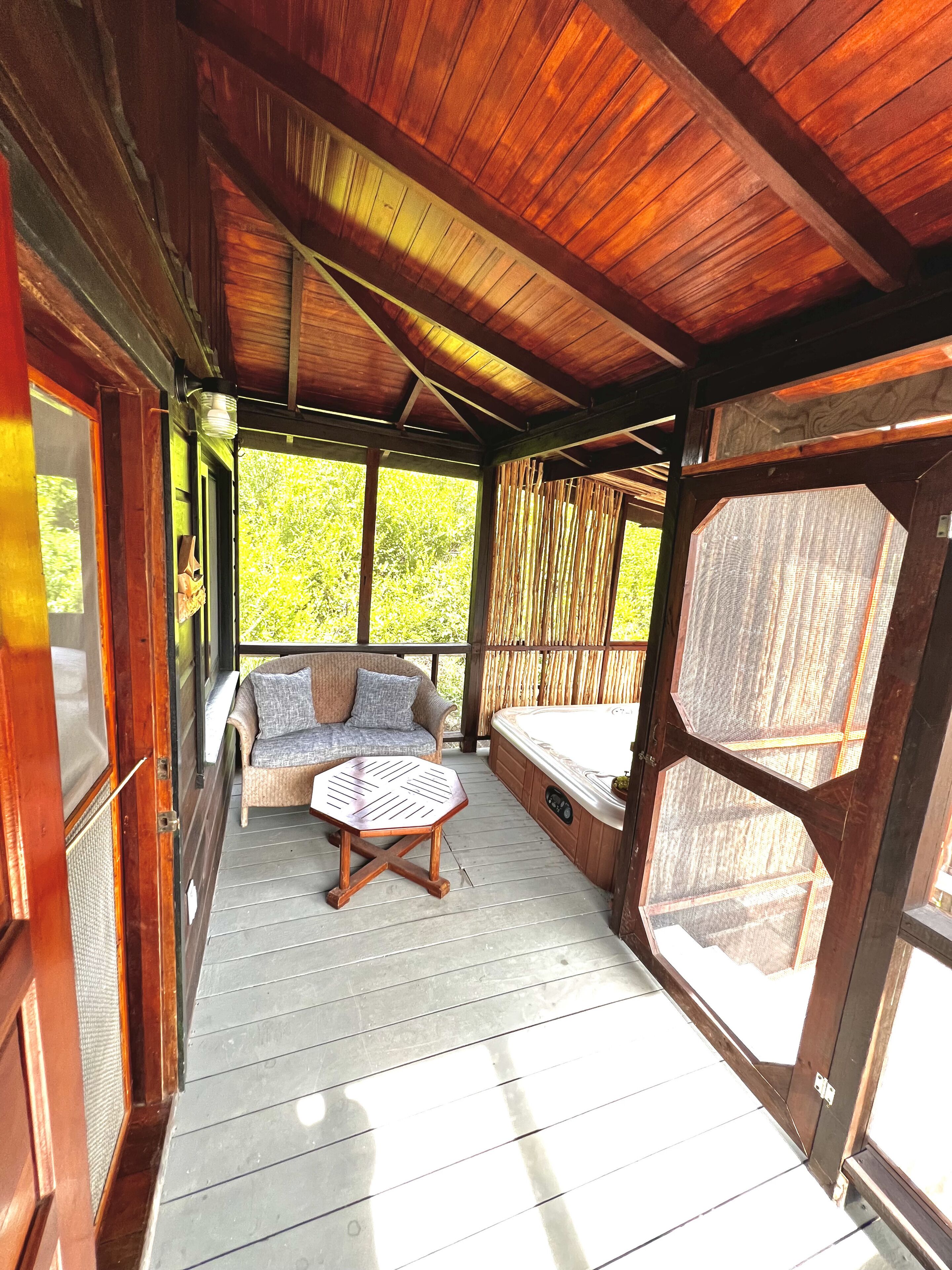 Une véranda couverte avec un plafond en bois, un canapé en osier, une petite table et un jacuzzi.