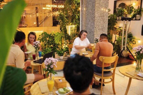 Um grupo de pessoas jantando em um restaurante com mesas, cadeiras e plantas em vasos.