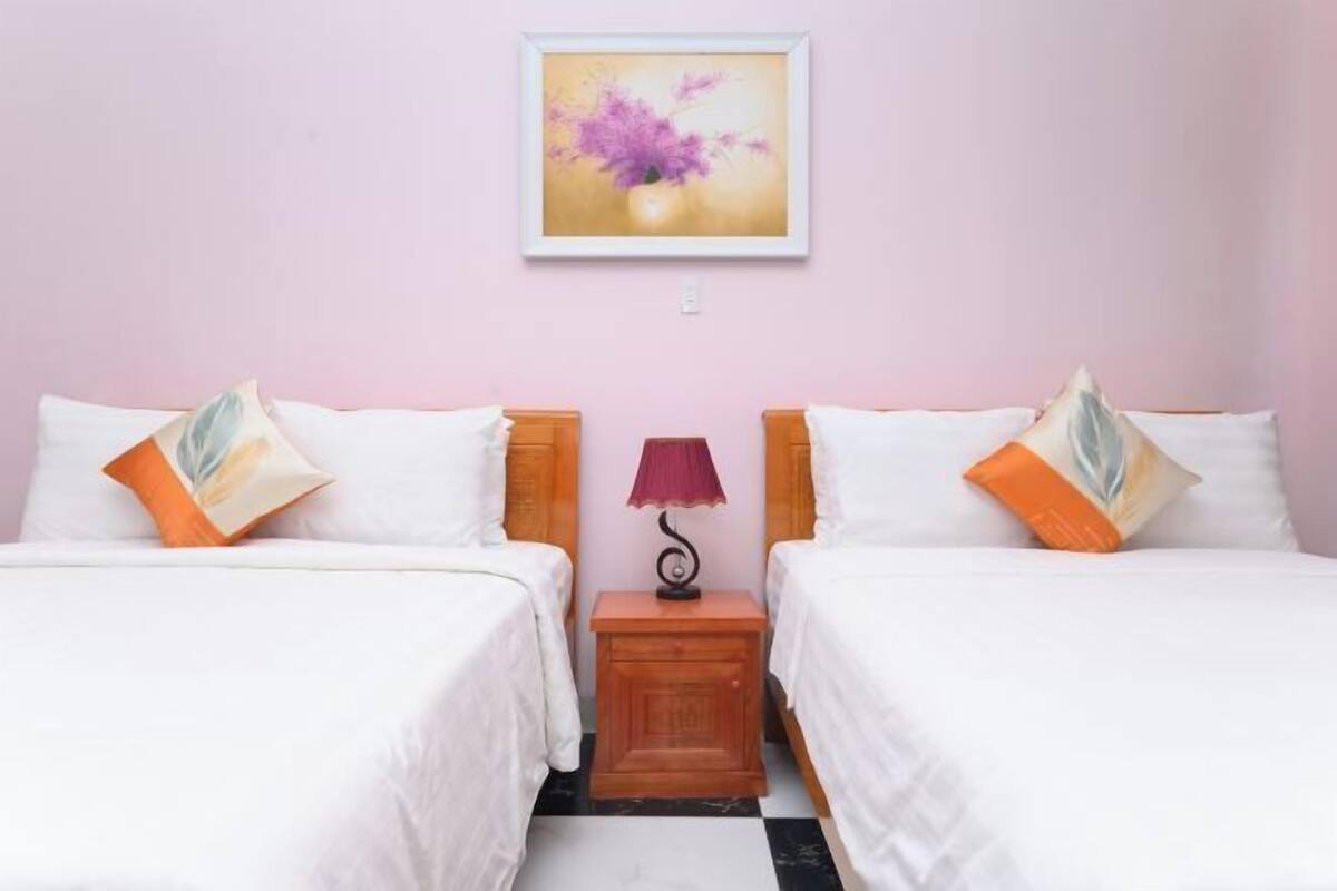 A double room with two beds, a nightstand with a lamp, and a framed picture on the wall.
