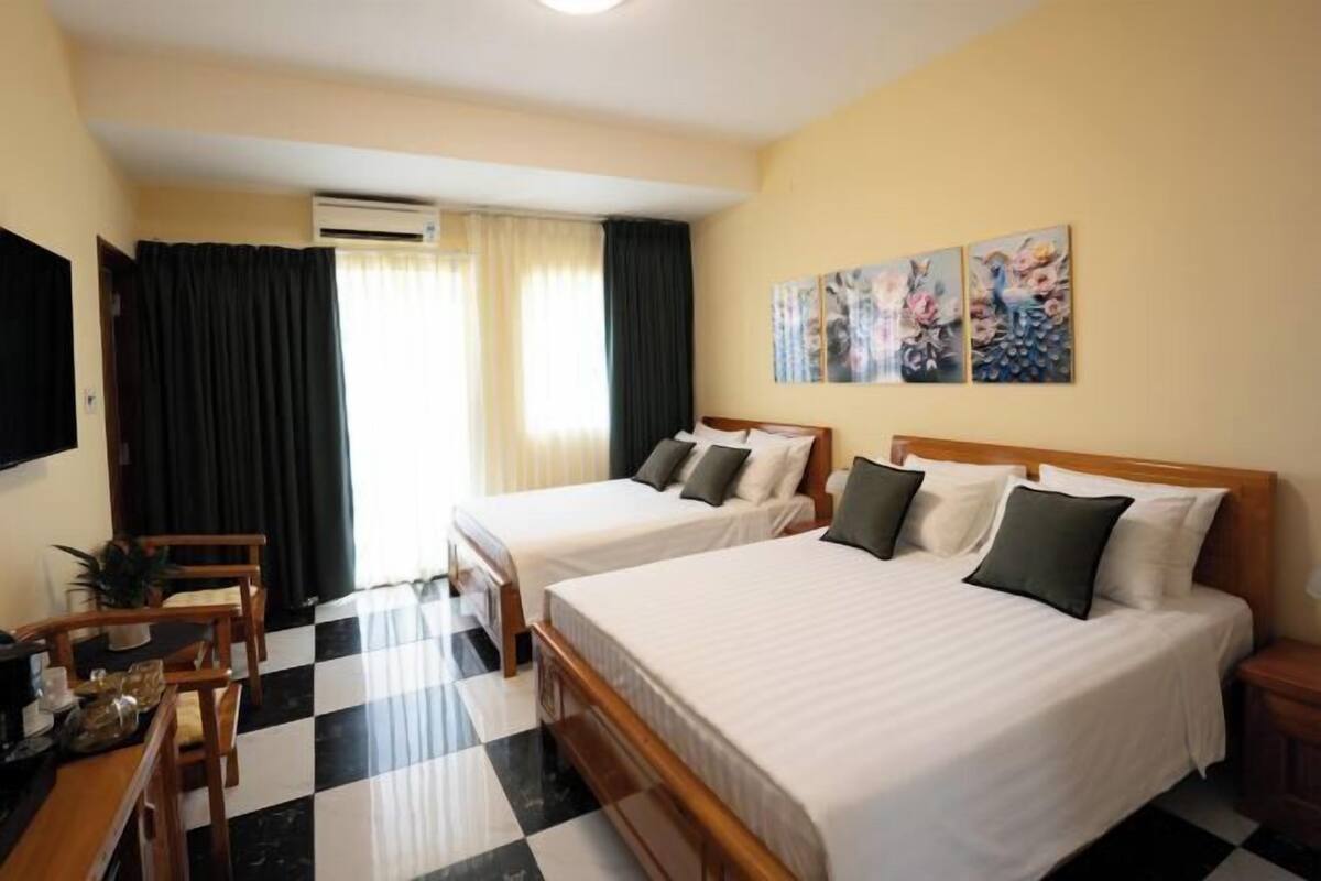 A hotel room with two beds, a desk with chairs, a flat-screen TV, and artwork on the wall.