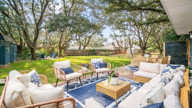 An outdoor patio with wicker furniture, a blue patterned rug, and a potted plant.