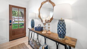 A hallway with a wooden door, a console table with decorative lamps, a mirror, and a small clock.