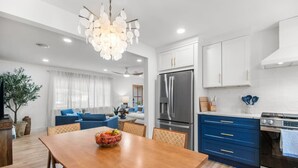 A modern kitchen with a dining area, featuring a large wooden table, a chandelier, and stainless steel appliances.