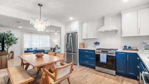 A modern kitchen with white and blue cabinets, stainless steel appliances, and a wooden dining table.