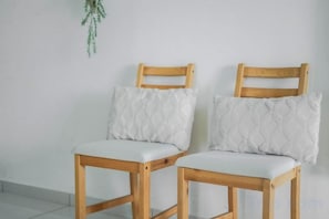 Two wooden chairs with cushioned seats and backrests, positioned against a plain wall with a hanging plant. - Beacon Executive Suites by Simply Penang (George Town)