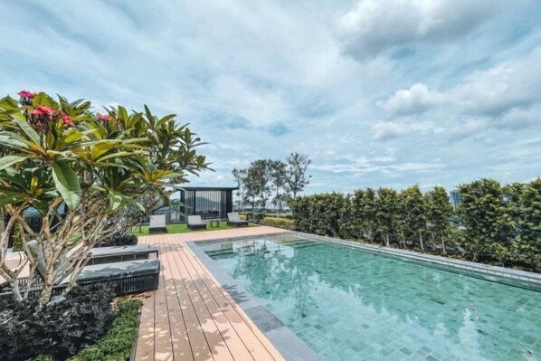 A swimming pool with a wooden deck, surrounded by greenery and a gazebo. - Beacon Executive Suites by Simply Penang (George Town)