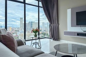 A modern living room with a large window, a flat-screen TV, a round glass table, and a sofa. - Beacon Executive Suites by Simply Penang (George Town)