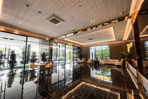 A modern hotel lobby with a reflective black marble floor, large windows offering a view of greenery, and contemporary furniture. - Beacon Executive Suites by Simply Penang (George Town)