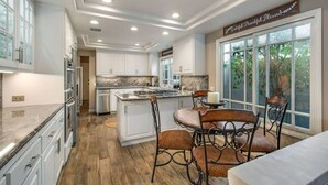 A spacious kitchen with white cabinets, a granite countertop, and a dining area with a table and chairs. - Seascape Estate - Steps To Harbor Beach, Pool, Spa (Huntington Beach)
