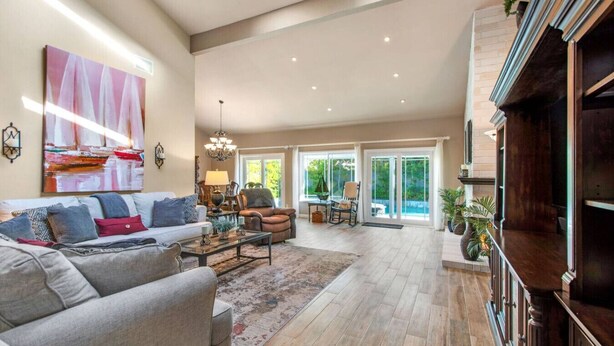 A spacious living room with a large sofa, a coffee table, and a fireplace. There is a dining area with a table and chairs, and a view of the outdoors through large windows. - Seascape Estate - Steps To Harbor Beach, Pool, Spa (Huntington Beach)