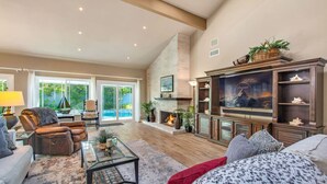 A spacious living room with a fireplace, comfortable seating, and a large television. - Seascape Estate - Steps To Harbor Beach, Pool, Spa (Huntington Beach)