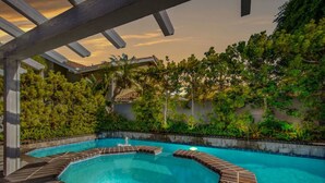 A swimming pool with a geometric design, surrounded by lush greenery and a pergola structure. - Seascape Estate - Steps To Harbor Beach, Pool, Spa (Huntington Beach)