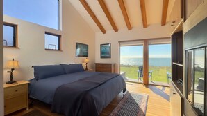A bedroom with a large bed, wooden beams, a view of the sea, and a balcony with chairs. - Seascape Oceanfront w/ hot tub, private courtyard (Sea Ranch)