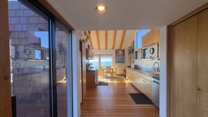 A modern kitchen with wooden beams, a dining area with a view, and a sliding glass door leading to an outdoor area. - Seascape Oceanfront w/ hot tub, private courtyard (Sea Ranch)