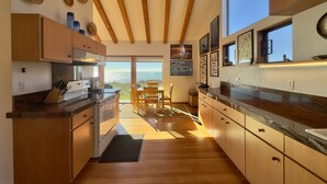 A modern kitchen with wooden cabinets, a large window, and a dining area with a view. - Seascape Oceanfront w/ hot tub, private courtyard (Sea Ranch)