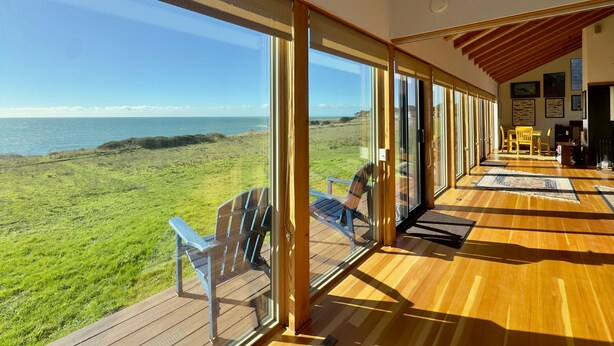 A room with large windows overlooking a grassy area and the sea. There are wooden floors and a ceiling with wooden beams. - Seascape Oceanfront w/ hot tub, private courtyard (Sea Ranch)
