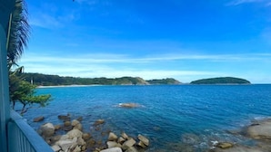 Blick auf die Küste mit klarem, blauem Wasser, felsigem Ufer und grünen Hügeln im Hintergrund.