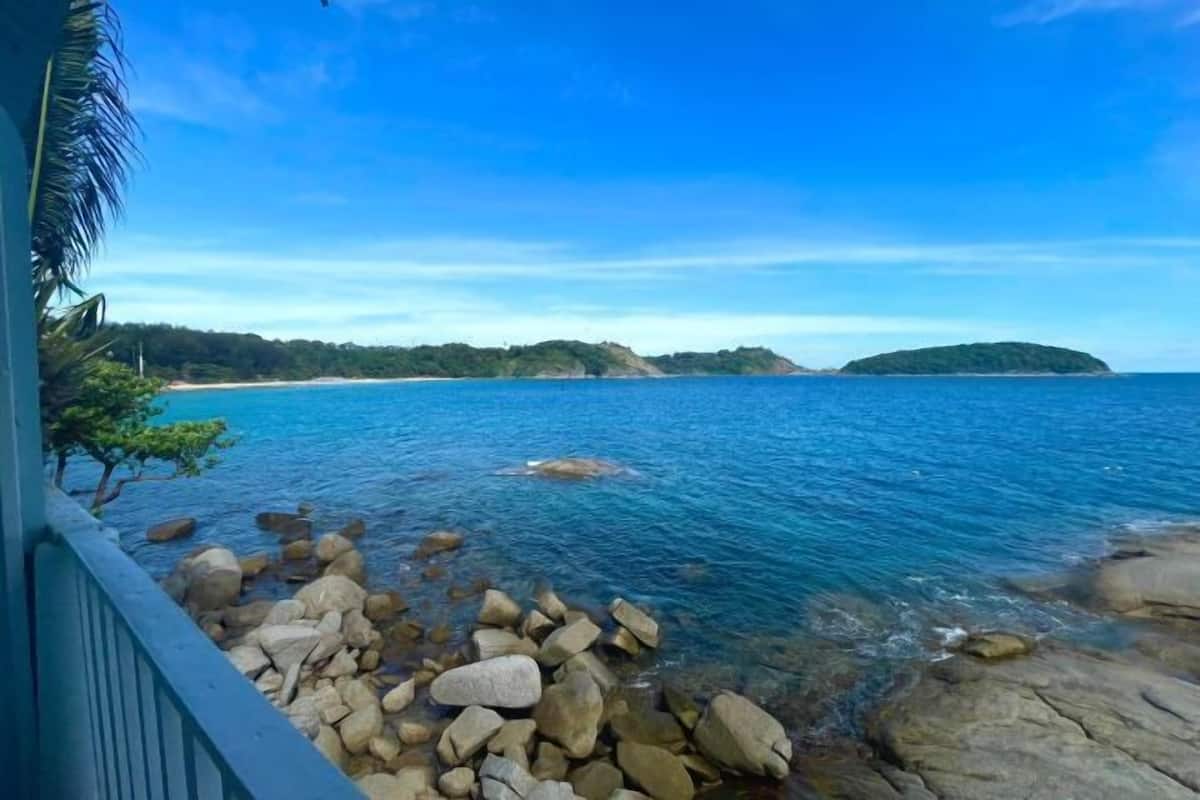 Une vue sur la côte, avec une eau d’un bleu limpide, un rivage rocheux et des collines verdoyantes à l’horizon.