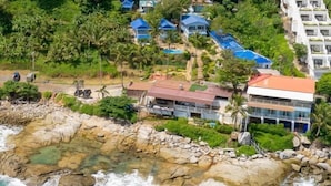 Ein Küstenhotel mit mehreren Gebäuden mit blauen Dächern, felsiger Küstenlinie und üppiger Vegetation.