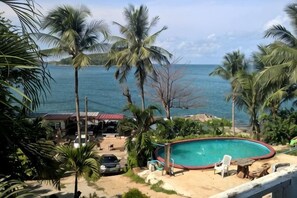 A pool with a view of the sea, surrounded by palm trees and a building with a red roof. - Naiharn on the Rock Resort Phuket (Phuket)