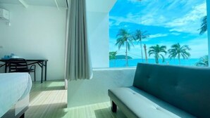 Ein Hotelzimmer mit Bett, einer Couch, einem Tisch und Blick auf Palmen sowie das Meer.