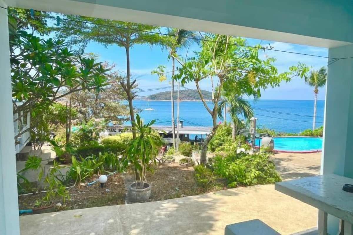 Un balcon avec vue sur la mer, entouré de verdure et donnant sur une piscine.