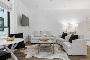 A modern living room with a sofa, armchairs, a coffee table, and a TV mounted on the wall. - Downtown Loft Walkable Regions Field, Restaurants (Birmingham)