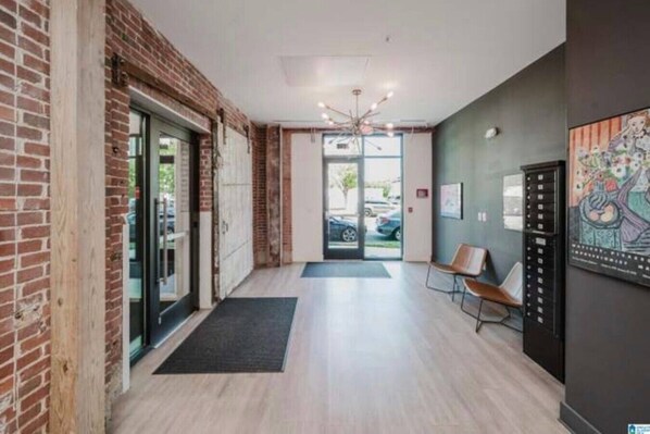 A modern lobby with a brick wall, a glass door entrance, a chandelier, and a seating area.