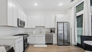 Una cocina moderna con armarios blancos, un refrigerador de acero inoxidable, una estufa y un lavavajillas.