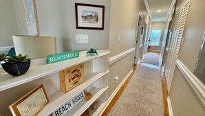 A hallway with a carpet, white walls, and shelves with signs reading "BEACH HOUSE."