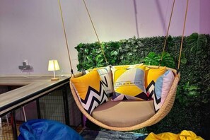 A hanging chair with cushions, a lamp, and a green wall with plants. - Swing & Pillows @ Beach Street (Northeast Penang Island)