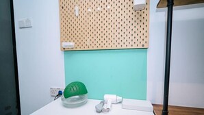 Une pièce avec une table blanche, un mur vert, un panneau perforé et un chapeau vert posé sur la table.