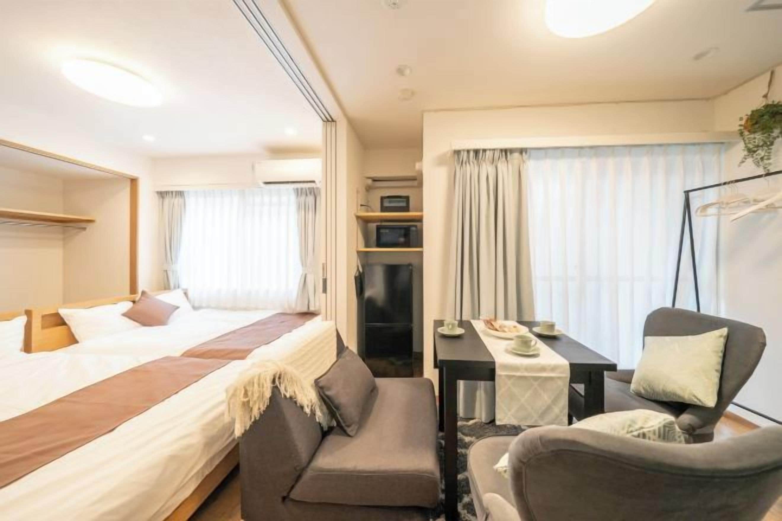 A hotel room with a bed, a sofa, a table with a chair, a TV, and a window with curtains.