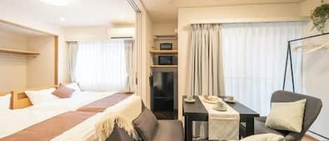 Una habitación de hotel con cama, sofá, mesa con silla, televisión y ventana con cortinas.