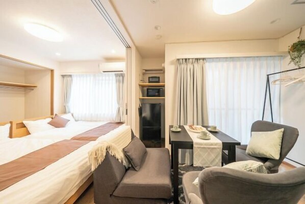 Una habitación de hotel con cama, sofá, mesa con silla, televisión y ventana con cortinas.