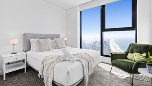 A modern bedroom with a large bed, a nightstand, a green armchair, and a large window offering a city view. - Cozy 2 Bedroom 2 Bathroom Ocean View Unit - Q Stay (Surfers Paradise)