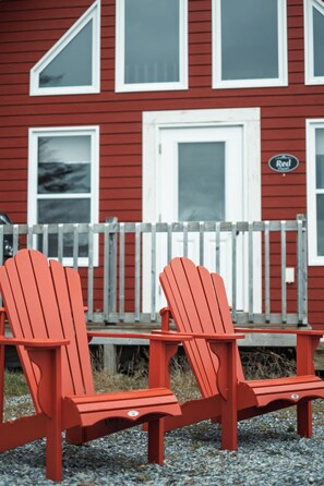To røde Adirondack-stole foran en rød bygning med hvid detaljering og et skilt med teksten 'Red'.