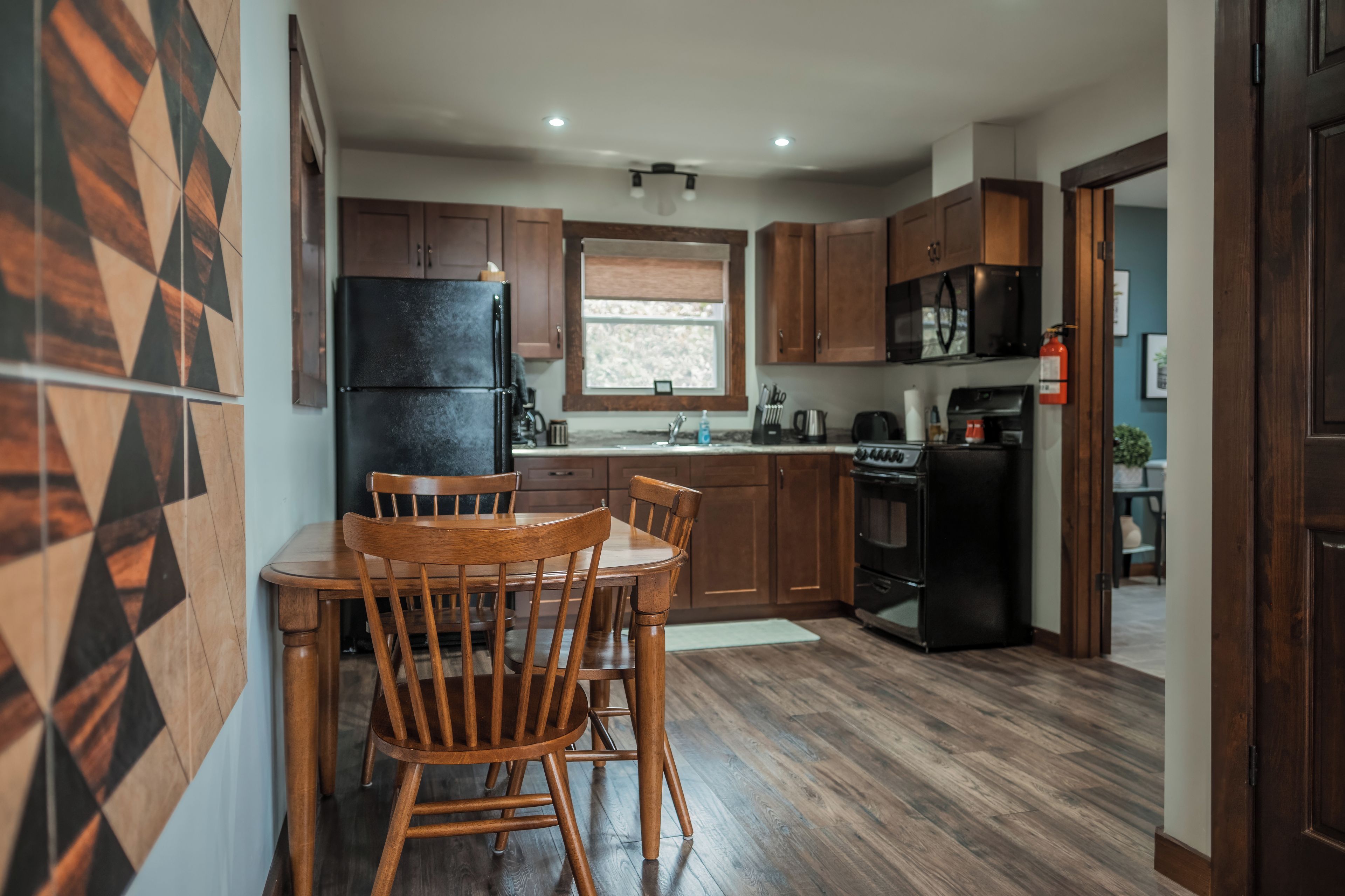 A modern kitchen with wooden cabinets, a black refrigerator, a stove, and a dining area with two wooden chairs.