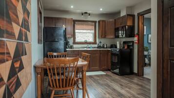 A modern kitchen with wooden cabinets, a black refrigerator, a stove, and a dining area with two wooden chairs.