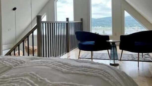 A bedroom with a large bed, a view of the outdoors through a window, and a staircase leading to an upper level.
