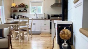 A modern kitchen with white cabinets, a dining area with wooden chairs, and a globe on a shelf.