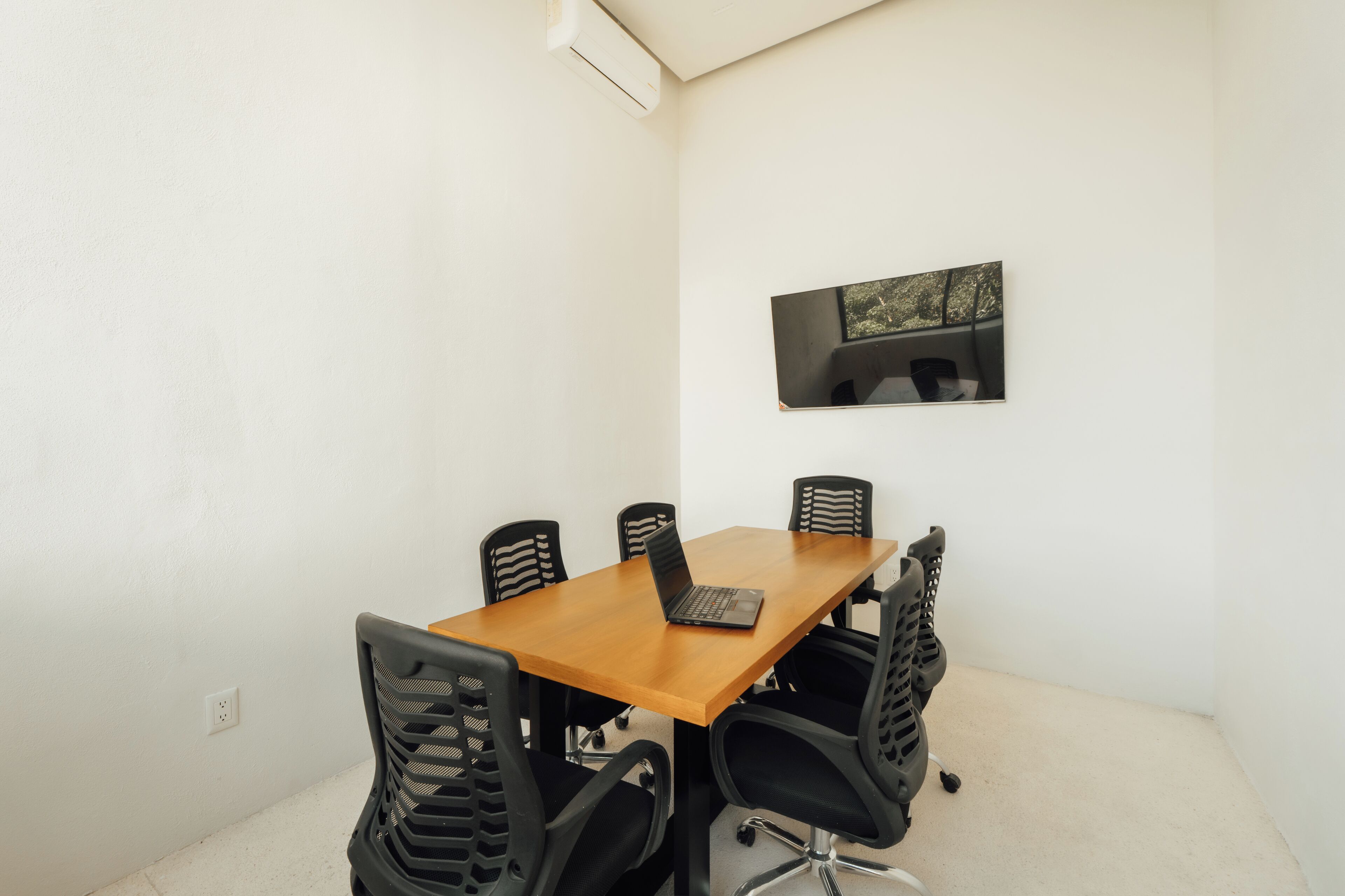 A conference room with a wooden table, six black chairs, and a laptop on the table.
