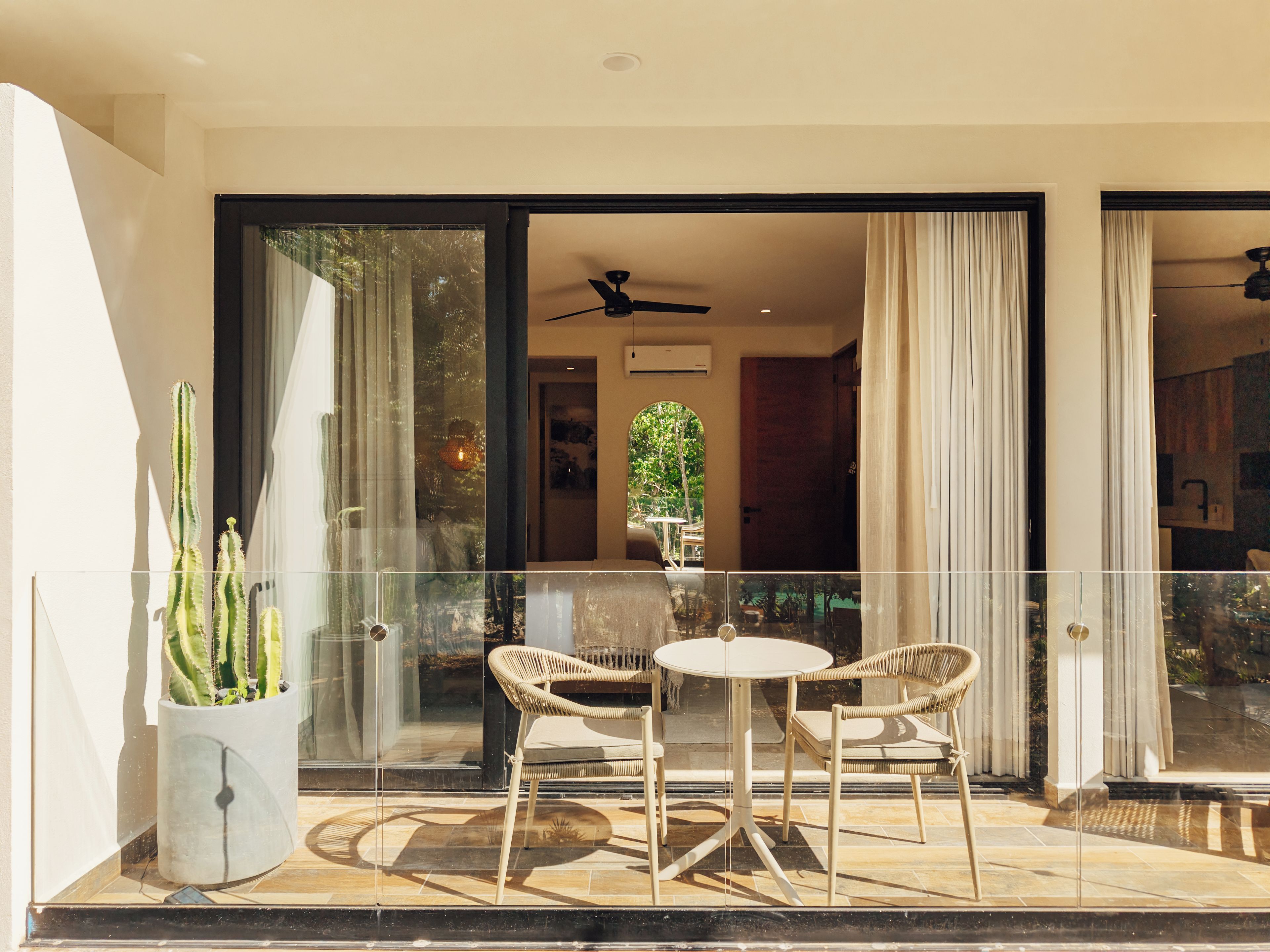 A glass-enclosed balcony with a table and chairs, a potted plant, and a ceiling fan.