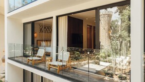 A balcony with two wooden chairs, a glass railing, and a view of a garden and building. - 101 Park Tulum by Lumina (Tulum)