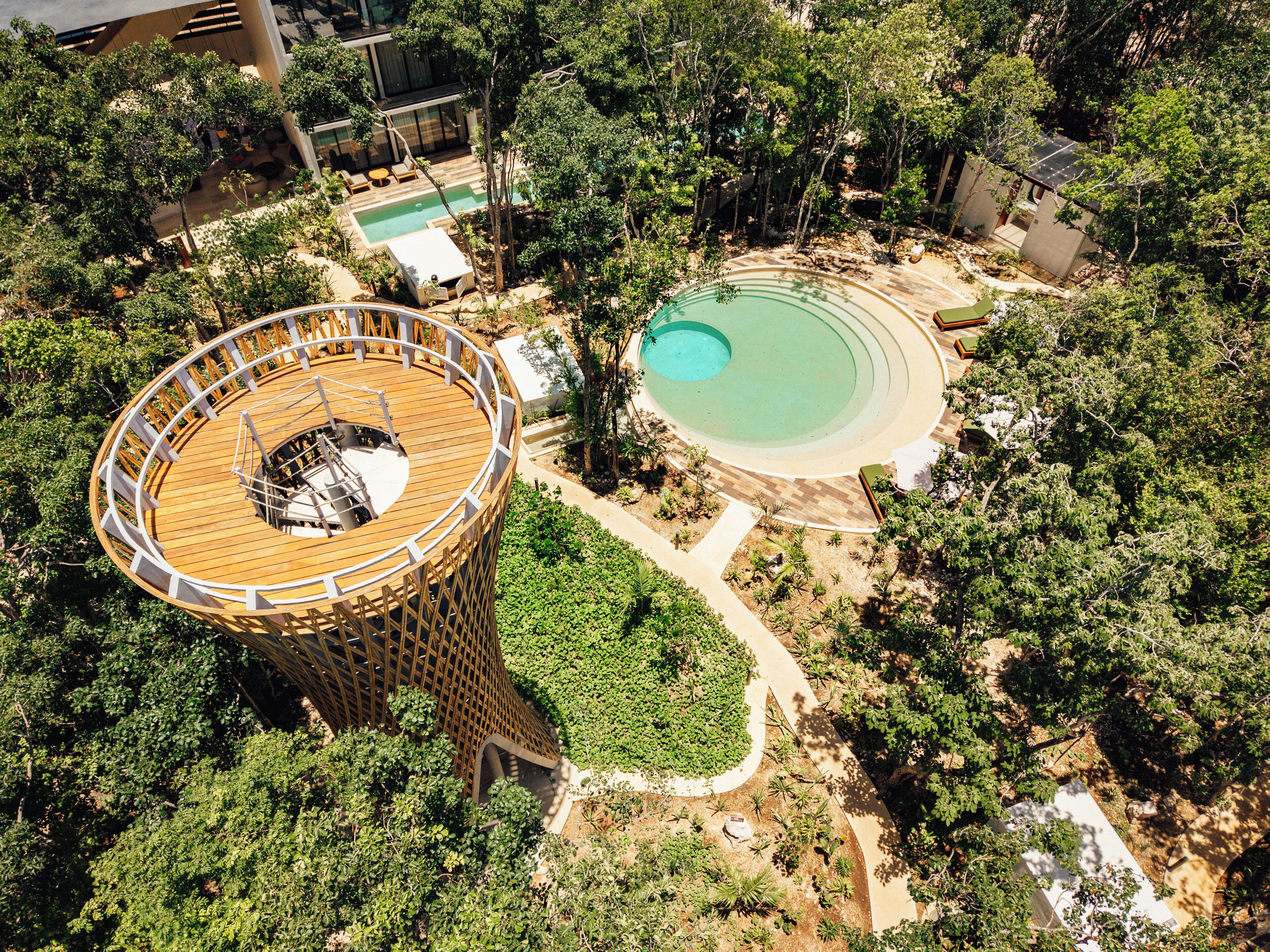 An aerial view of a resort with a large wooden deck, a circular pool, and surrounding greenery.