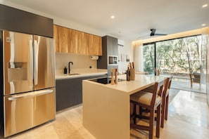 A modern kitchen with a central island, stainless steel appliances, and a view of the outdoors. - 101 Park Tulum by Lumina (Tulum)