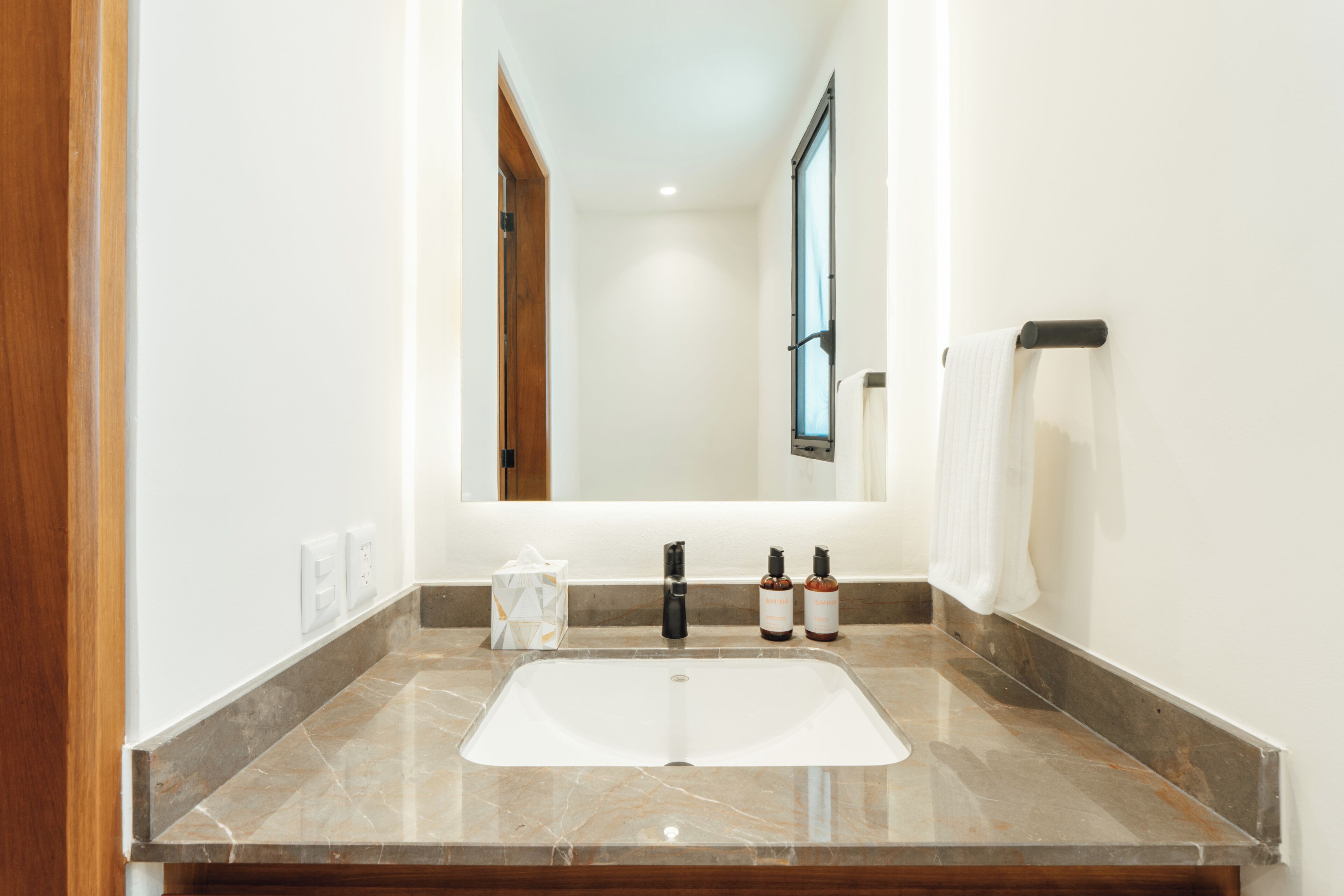 A bathroom with a white sink, a mirror, a towel rack, and two bottles on the counter.