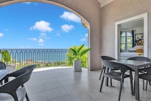Ein Balkon mit Meerblick, ausgestattet mit Korbstühlen und einem Tisch, sowie einem Blumentopf.