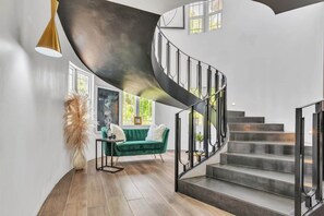Ein modernes Interieur mit einer Wendeltreppe, einem grünen Sofa und einer hohen Pflanze.